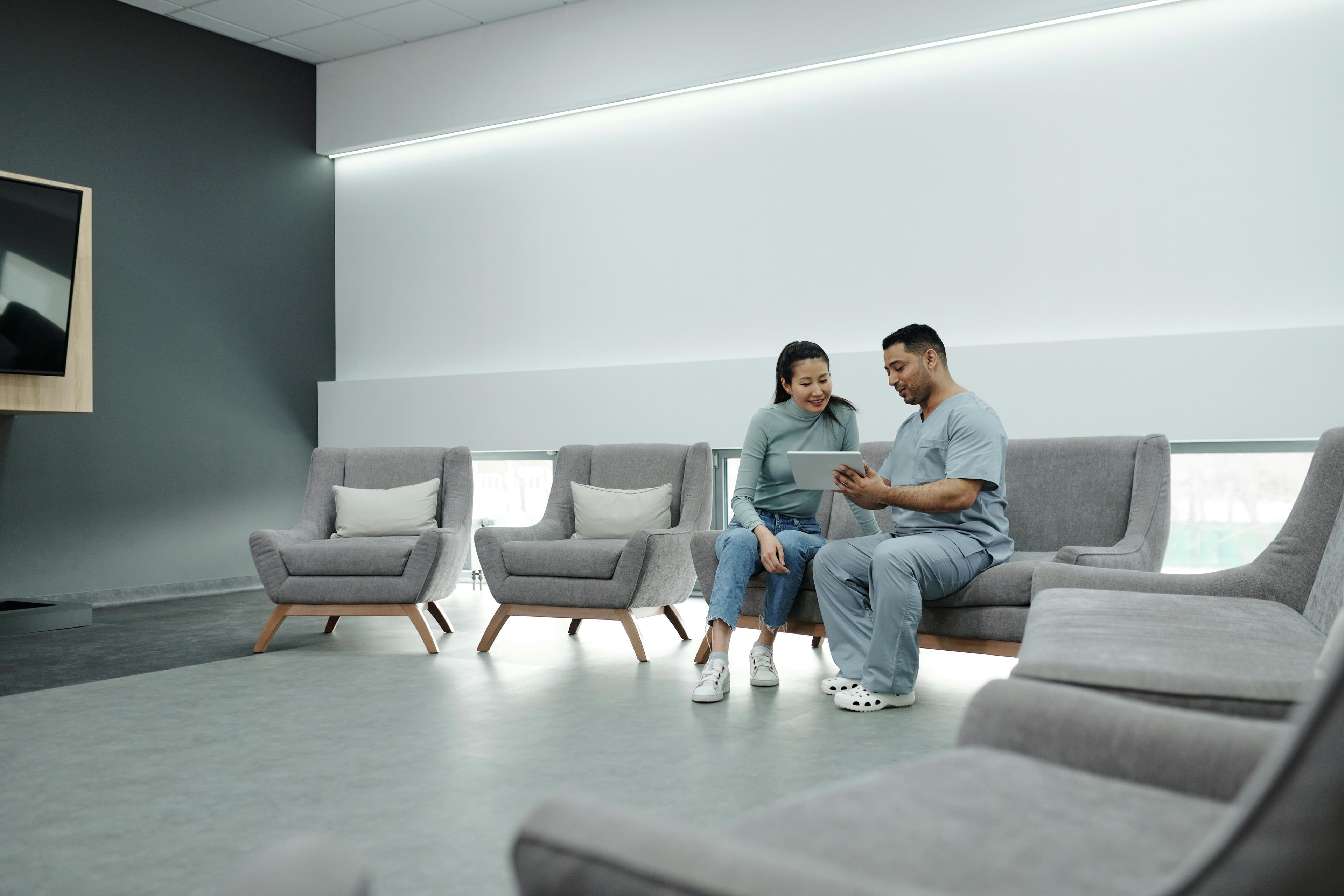 A doctor in scrubs consulting with a patient in a modern, indoor waiting area