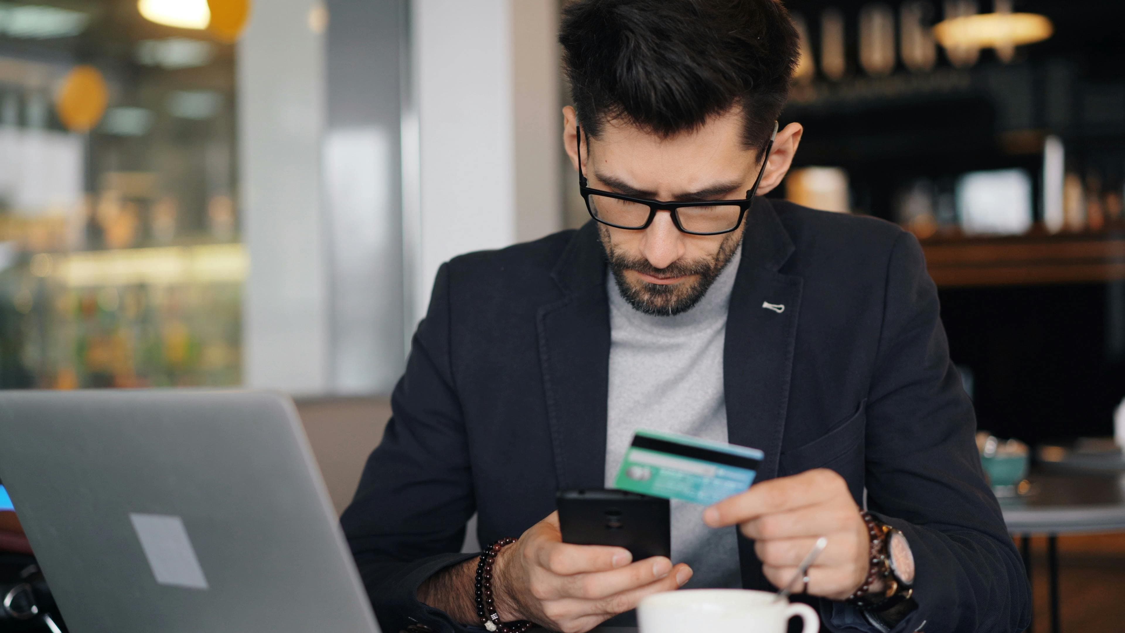 Businessman making online payment with smartphone and credit card in a modern café
