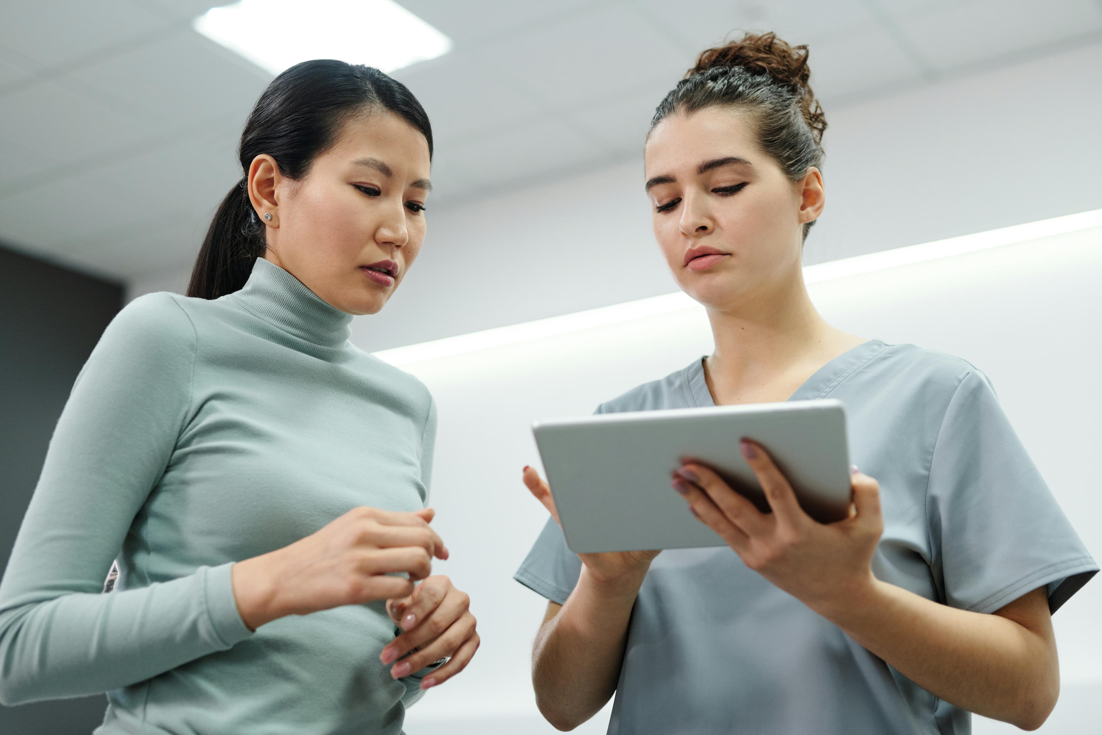 Two women engaged in a healthcare consultation using a digital tablet indoors